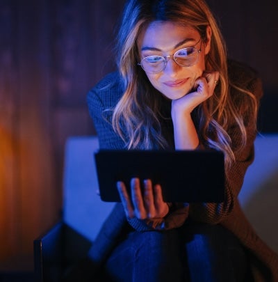Professional woman relaxing at home in the evening while using a tablet, representing healthy routines and unwinding after the workday.