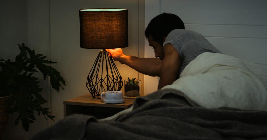 Man turning off a bedside lamp before sleep, representing healthy nighttime routines and preparing for restful sleep.