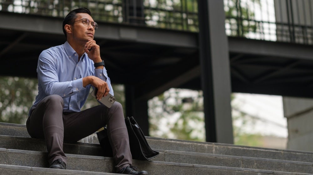 Thoughtful professional sitting on outdoor steps with a briefcase while considering next steps after leaving Federal service.