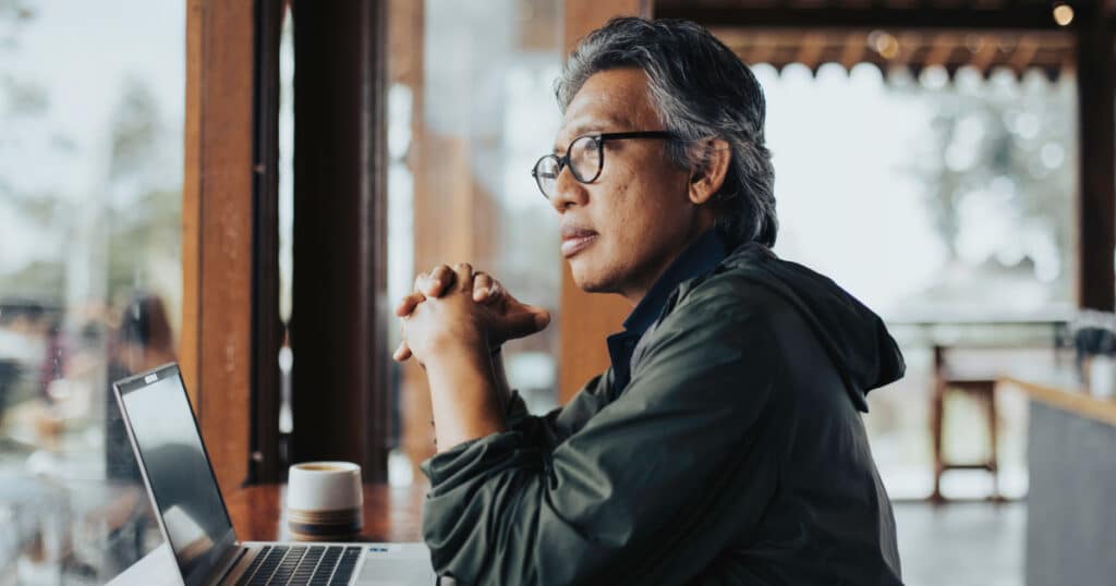 Experienced professional working on a laptop in a café while reviewing long-term financial and retirement plans.