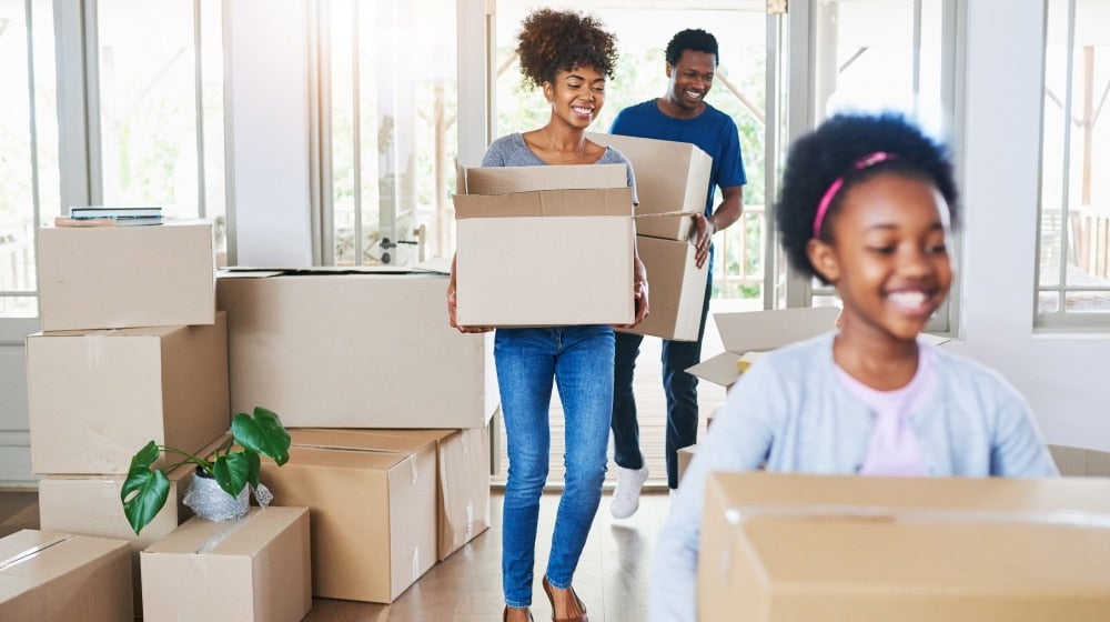 Federal employee family moving into a new home, carrying boxes during a relocation.
