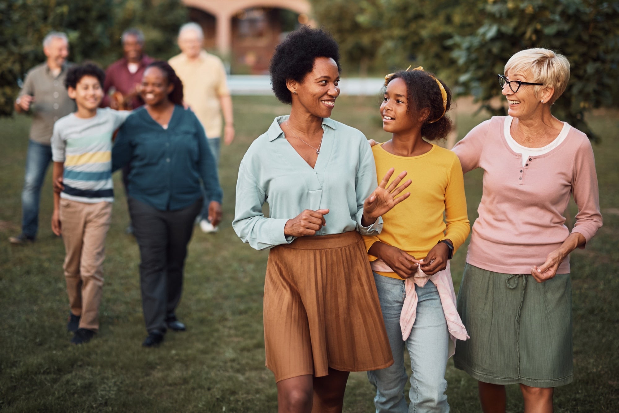 Group of diverse adults and a child walking together in a park, smiling and chatting as they stroll on the grass.